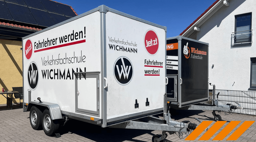 Zwei Fahrschule Wichmann Anhänger mit Werbung vor Gebäuden in Rastede