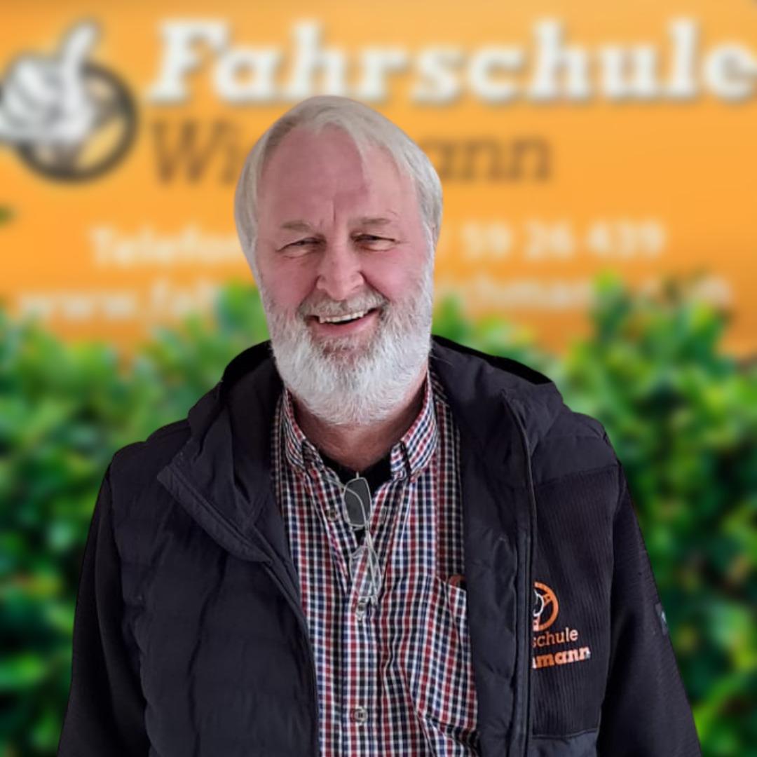 Fahrlehrer der Fahrschule Wichmann Rastede vor gelbem Hintergrund mit Logo