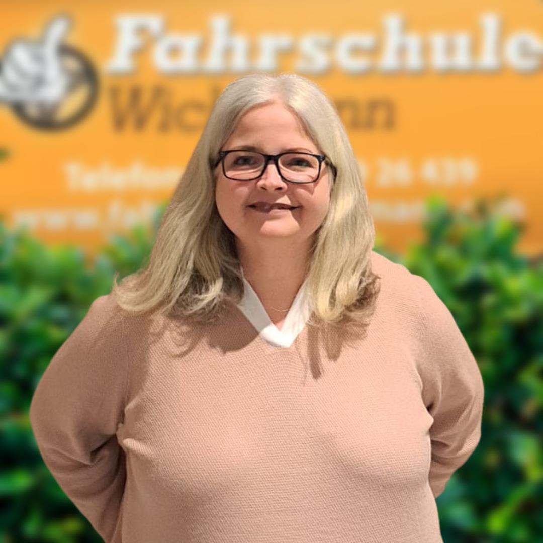 Frau mit Brille vor Fahrschule Wichmann Logo, freundlich und kompetent in Rastede
