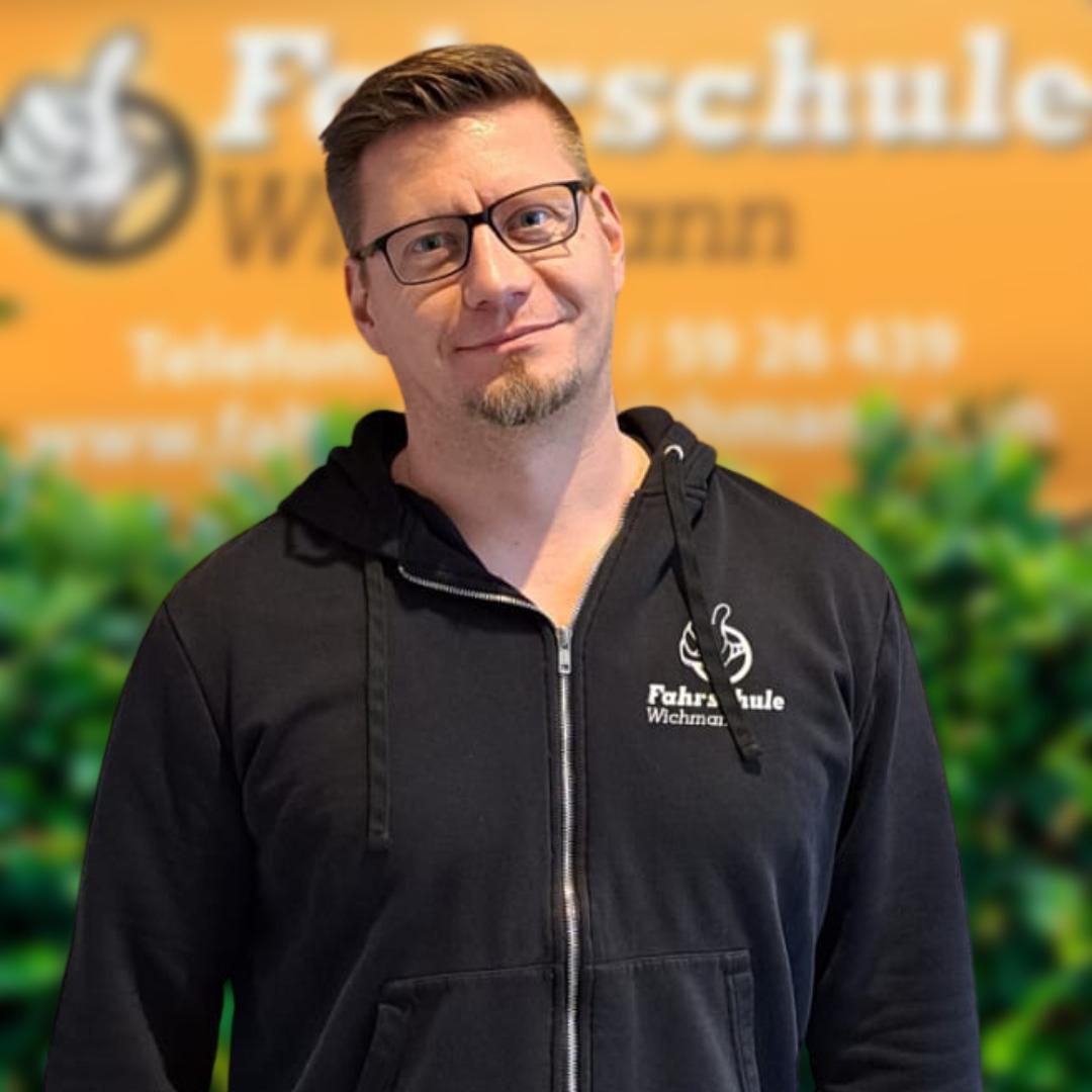Fahrlehrer der Fahrschule Wichmann mit Hoodie vor oranger Wand in Rastede