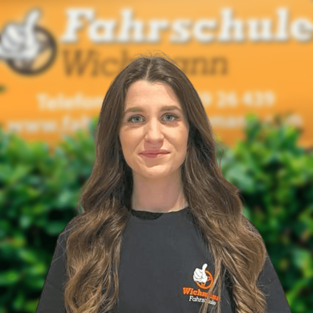 Mitarbeiterin der Fahrschule Wichmann Rastede vor einem orangen Schild mit Logo