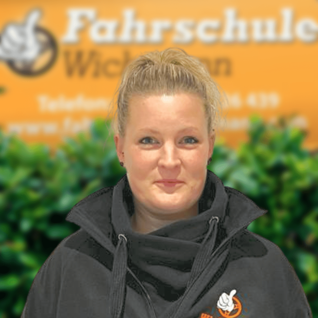 Lächelnde Mitarbeiterin der Fahrschule Wichmann Rastede im schwarzen Hoodie vor dem Logo