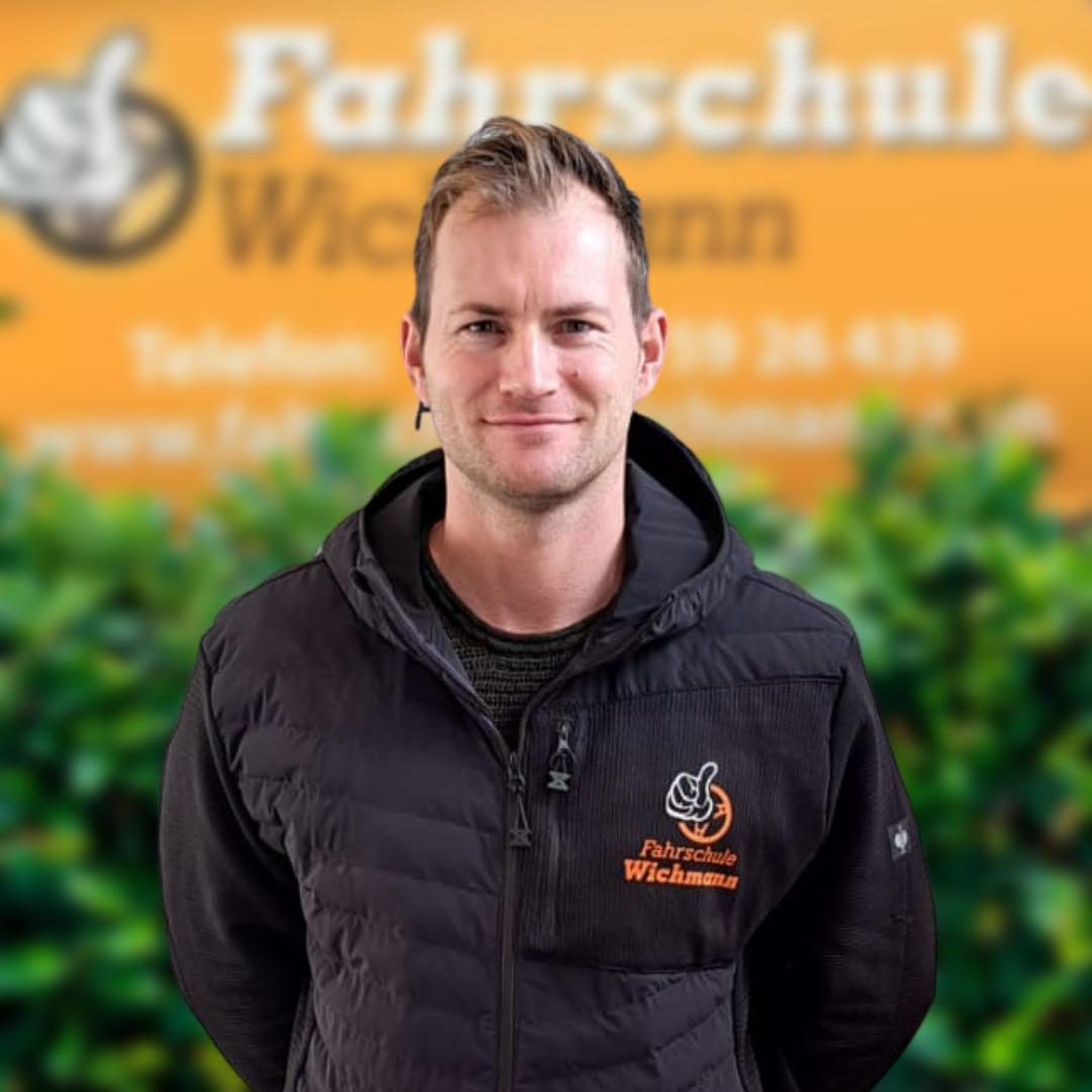 Fahrlehrer der Fahrschule Wichmann in Rastede mit Logo vor orangefarbenem Hintergrund
