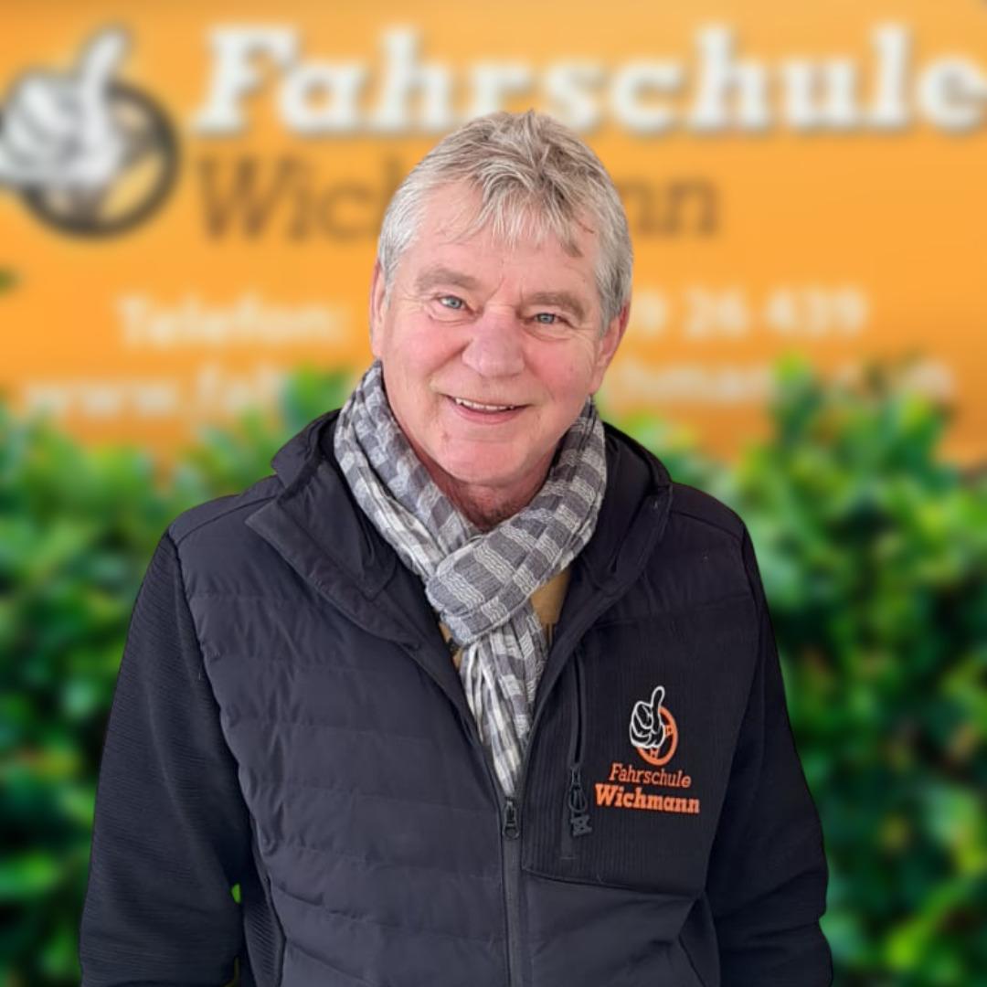 Fahrlehrer der Fahrschule Wichmann Rastede freundlich vor Firmenschild und grüner Hecke