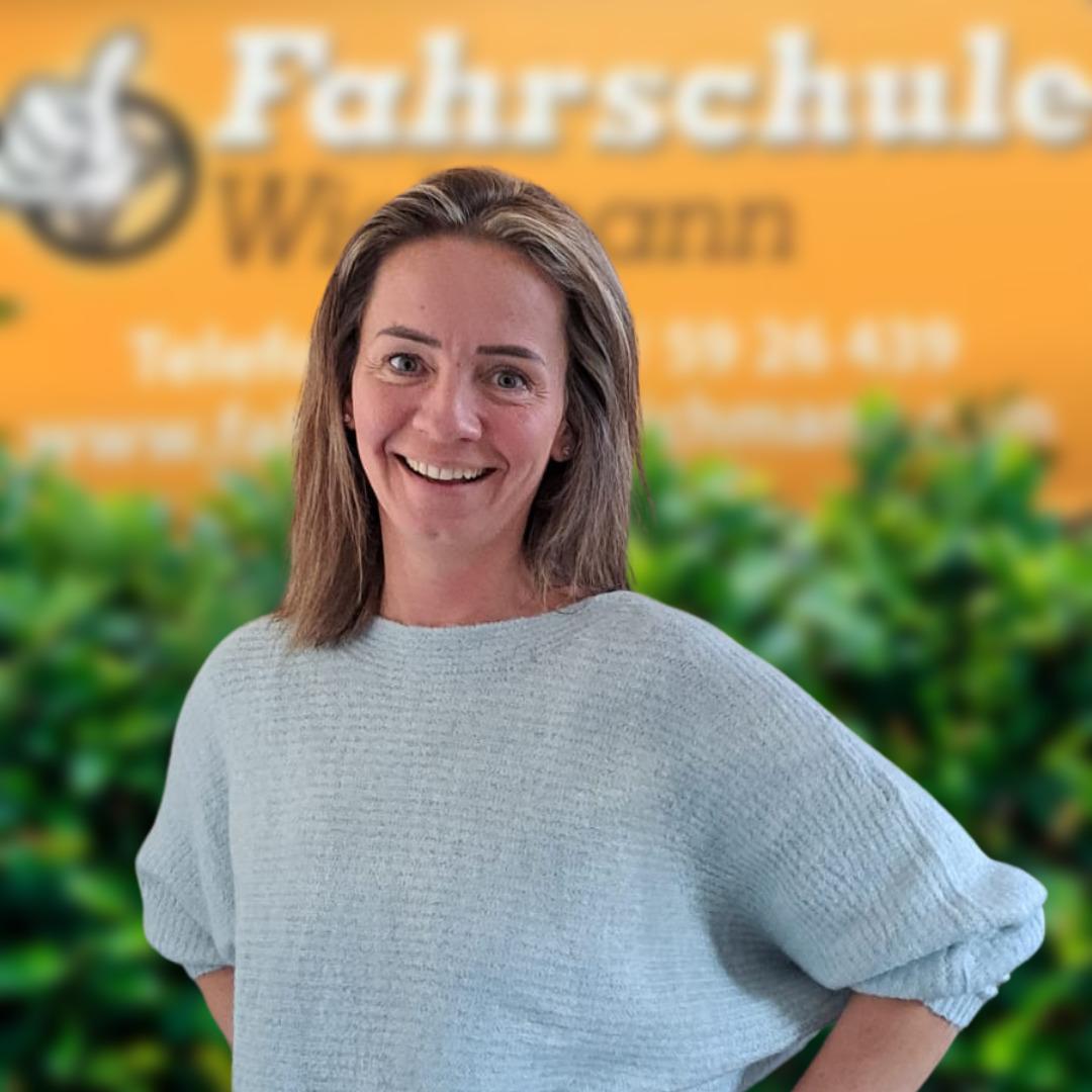 Lächelnde Mitarbeiterin der Fahrschule Wichmann Rastede vor grünem Hintergrund