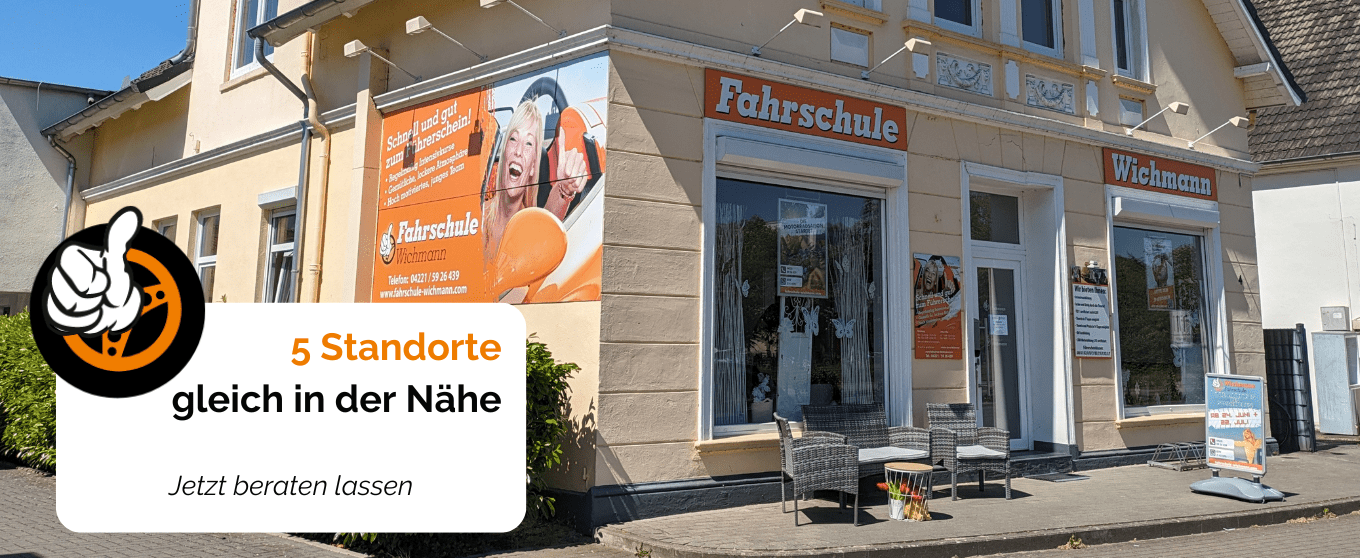 Fahrschule Wichmann Rastede mit großer Fensterfront, orange Schildern und Sitzmöbeln vor dem Eingang