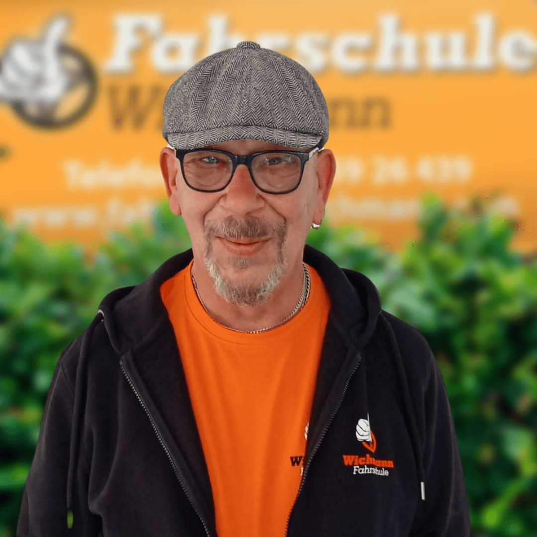 Fahrlehrer der Fahrschule Wichmann Rastede lächelt vor einem Firmenschild
