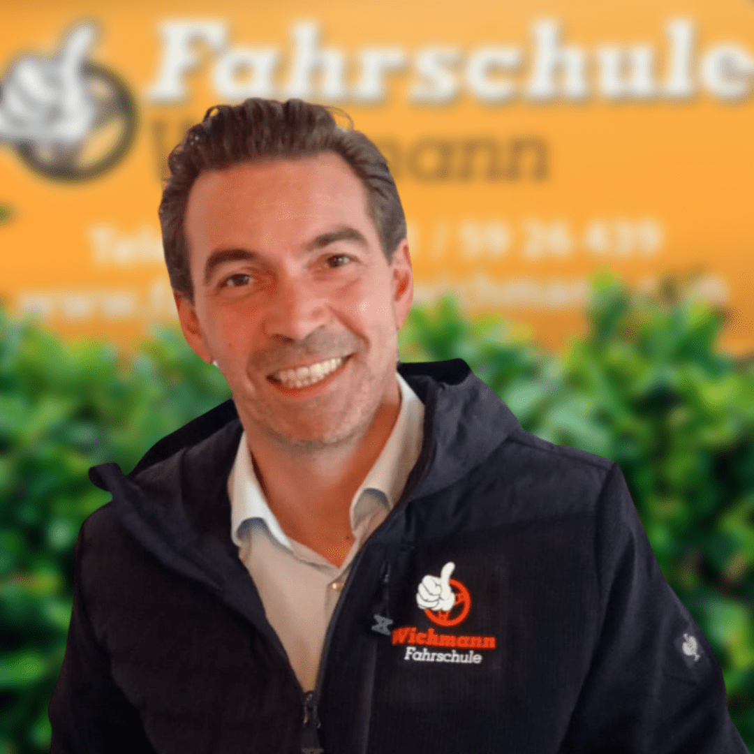Lächelnder Fahrlehrer der Fahrschule Wichmann Rastede steht vor gelbem Eingangsschild
