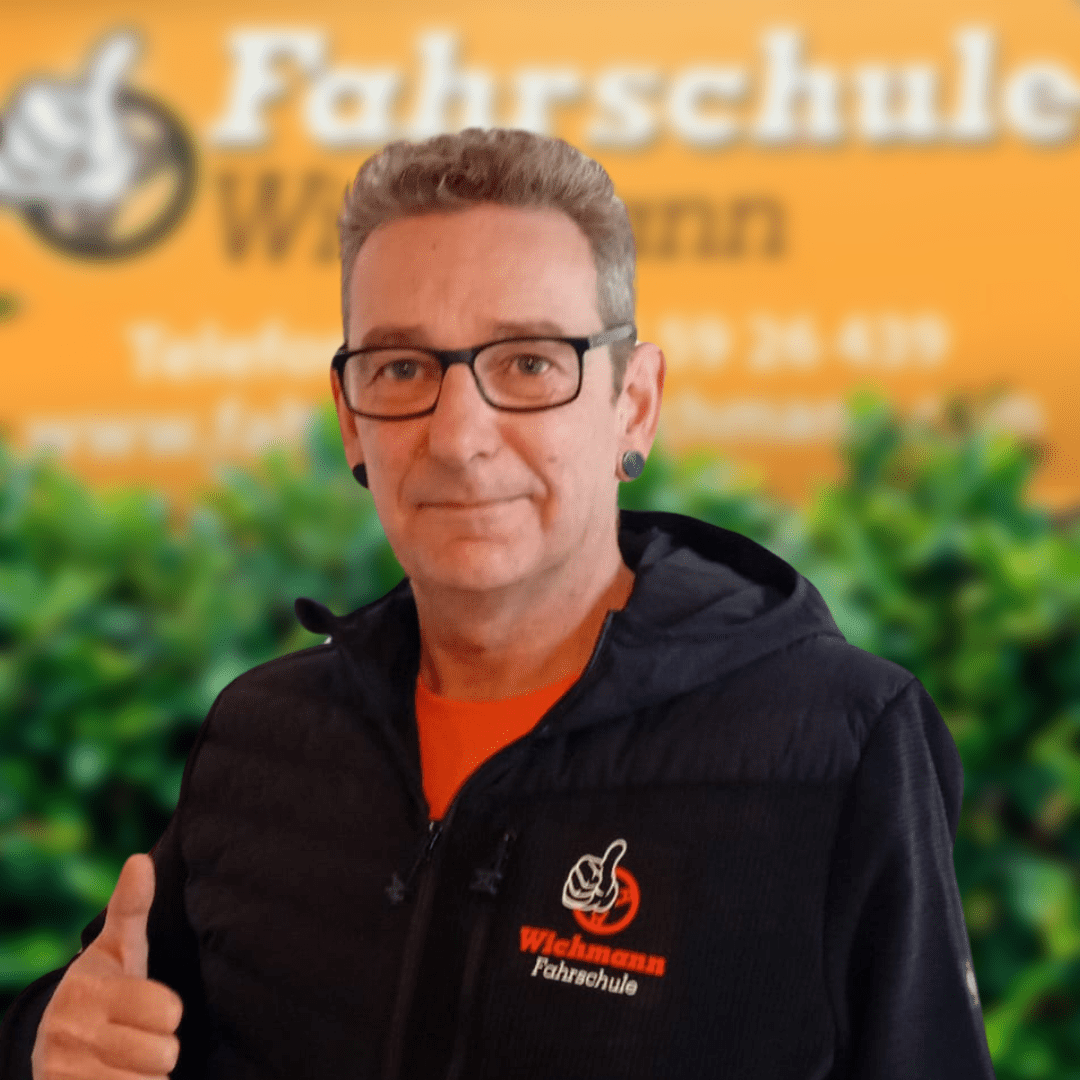 Fahrlehrer der Fahrschule Wichmann Rastede mit Daumen hoch vor Standort-Schild