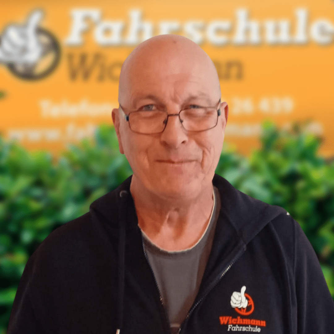 Fahrlehrer der Fahrschule Wichmann in Rastede mit Firmenlogo im Hintergrund
