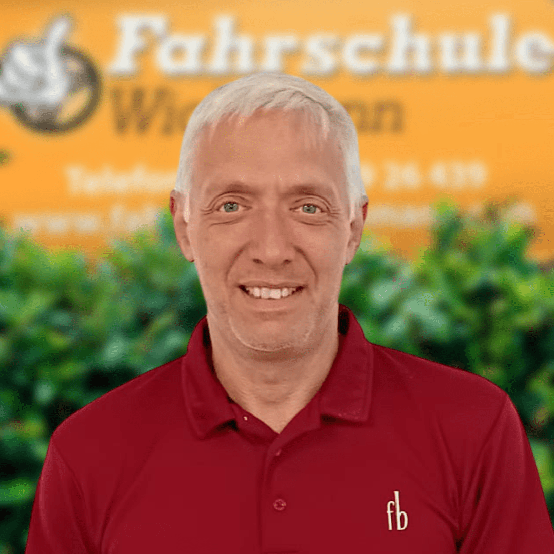 Fahrlehrer lächelt vor dem gelben Fahrschule Wichmann Schild in Rastede