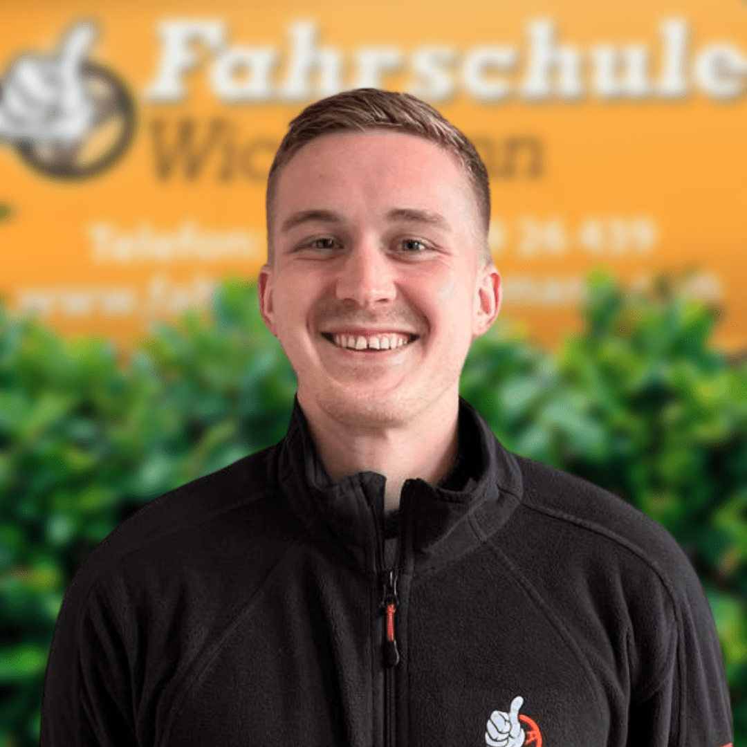 Fahrlehrer Jonas vor Logo der Fahrschule Wichmann in Rastede