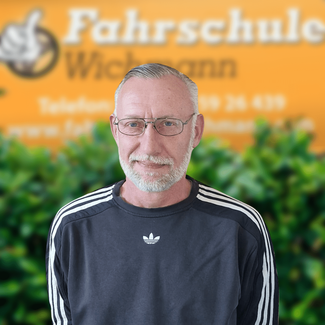 Fahrlehrer vor dem Schild der Fahrschule Wichmann Rastede mit grünem Hintergrund