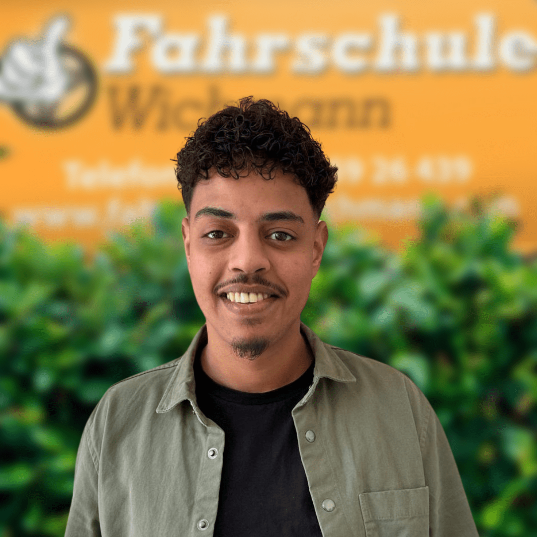 Fahrlehrer der Fahrschule Wichmann in Rastede vor grünem Hintergrund und gelbem Schild