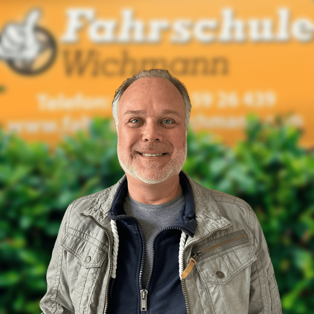 Fahrlehrer Sven lächelt vor Schild mit Logo der Fahrschule Wichmann in Rastede