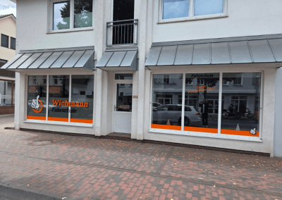 Außenansicht der Fahrschule Wichmann Rastede mit großen Fenstern und orangefarbenem Branding