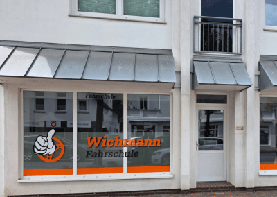 Fahrschule Wichmann Rastede mit Glasfront, Logo und Daumen-hoch-Grafik am Eingang